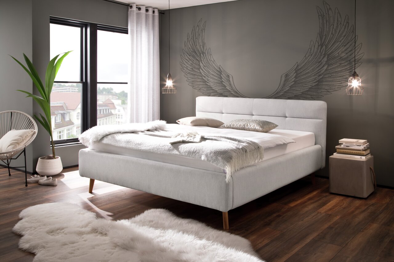 Modernes Polsterbett LOTTE in einem stilvollen Schlafzimmer mit grauer Wand und Flügelmotiv, seitliche Perspektive.