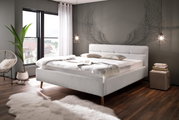 Modernes Polsterbett LOTTE in einem stilvollen Schlafzimmer mit grauer Wand und Flügelmotiv, seitliche Perspektive.