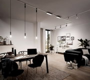 Moderne Wohnzimmerszene mit Schienensystem an der Decke, das mehrere Leuchten trägt. Perspektive von der Seite des Raumes mit Blick auf den Esstisch und das Wohnzimmer.