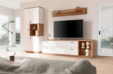 Modernes Highboard in einem Wohnzimmer, mit weißem und holzfarbenem Design, links neben einem großen Fernseher. Perspektive von der Couch aus.