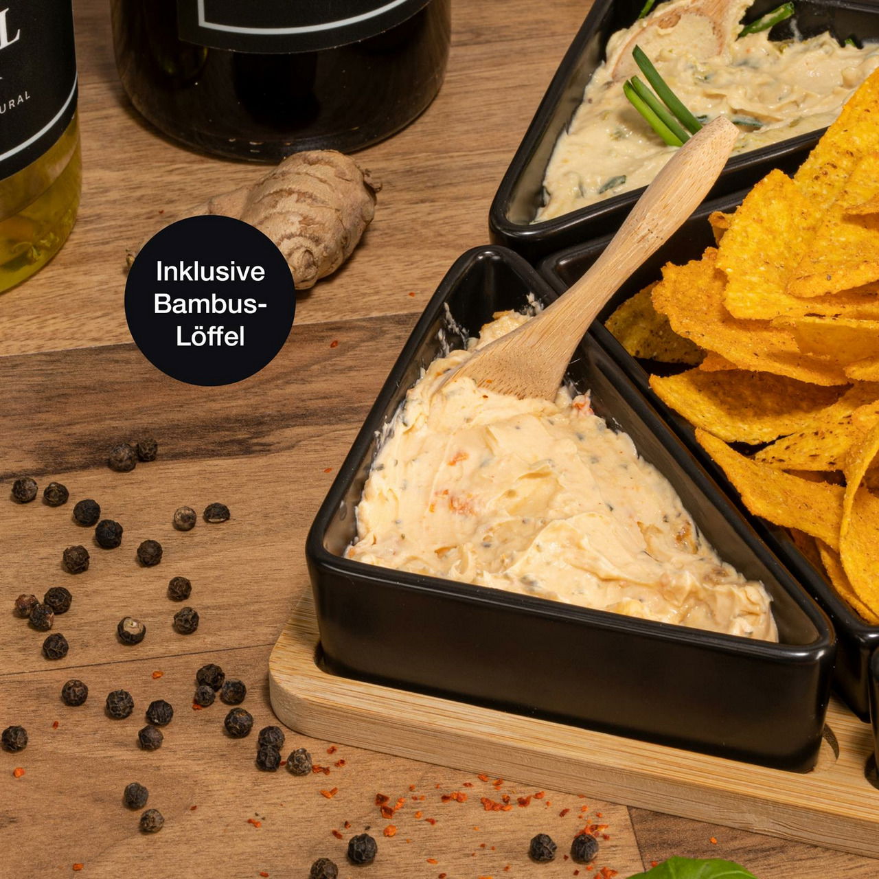 Nahaufnahme eines Serviersets aus Bambus mit fünf schwarzen Schalen, gefüllt mit Dips und Chips, inklusive Bambus-Löffel, auf einem Holztisch.