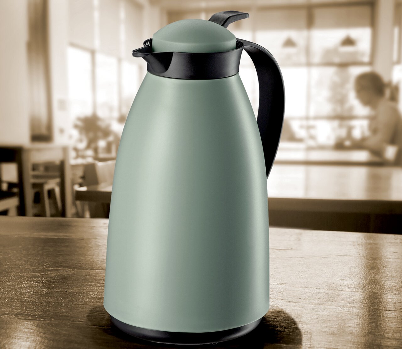 Cilio Isolierkanne 1L IMOLA Grüne matte Isolierkanne mit schwarzem Griff und Deckel, auf einem Tisch in einem Café aus seitlicher Perspektive.