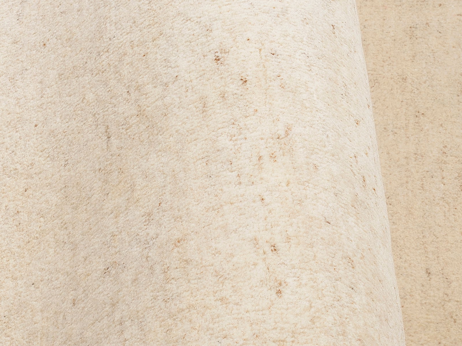 Nahaufnahme eines beigen Wollteppichs mit leichter Textur, seitliche Perspektive