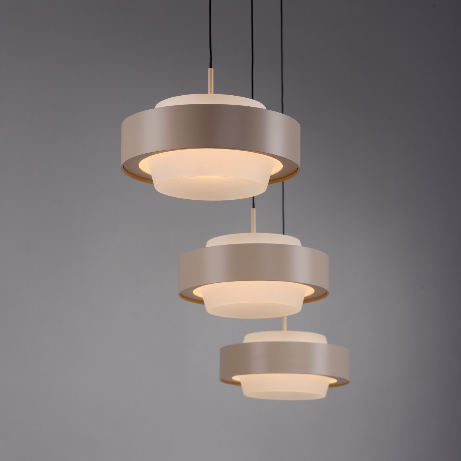 Drie moderne, cilindervormige hanglampen in matgrijs met een witte lichtverspreider, die een warm licht verspreiden, licht van bovenaf gezien tegen een grijze achtergrond