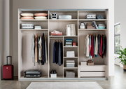 Offener Schwebetürenschrank mit zwei Türen, gefüllt mit Kleidung, Kissen und Accessoires, aus der Frontalperspektive fotografiert.
