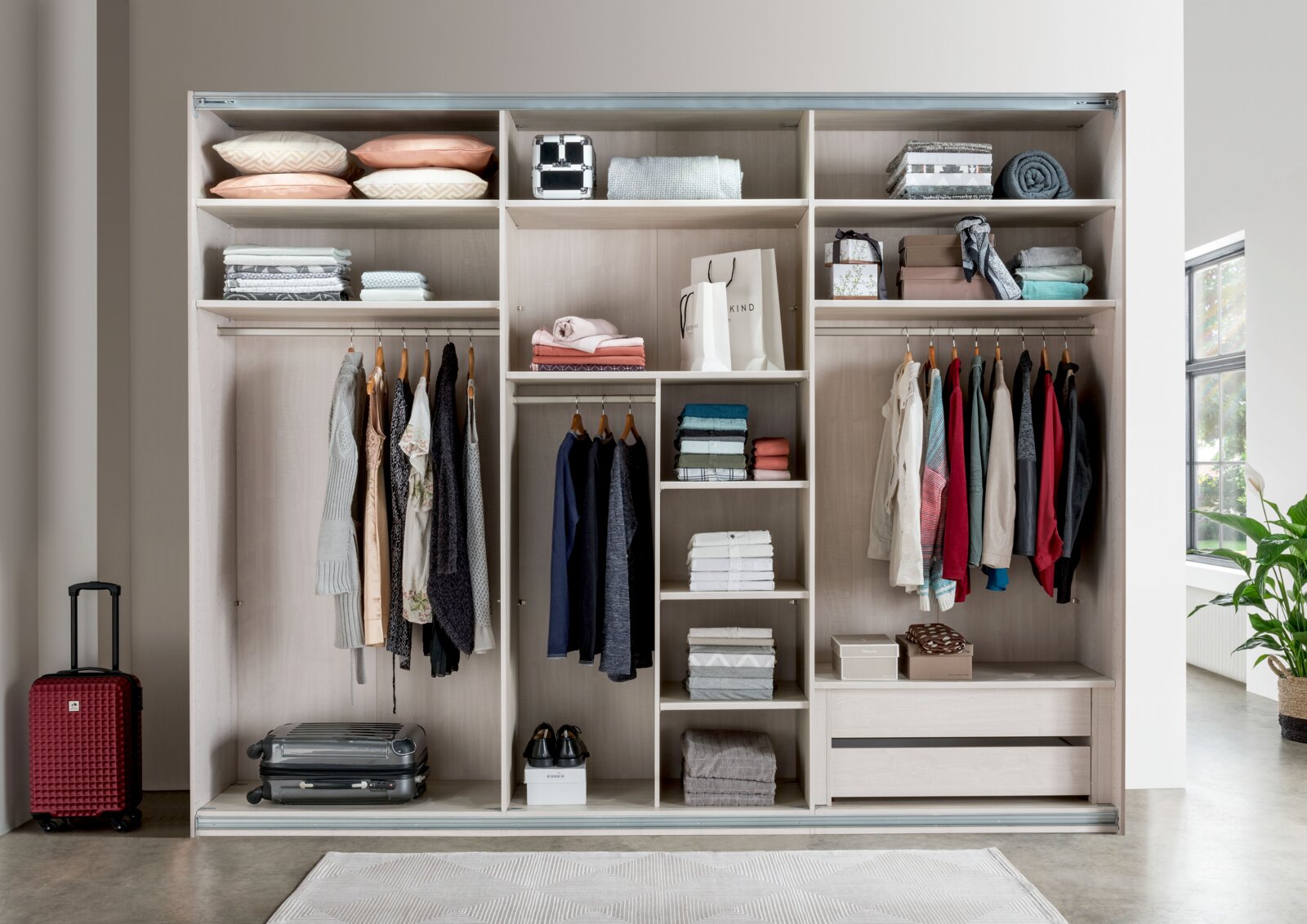 Offener Schwebetürenschrank mit zwei Türen, gefüllt mit Kleidung, Kissen und Accessoires, aus der Frontalperspektive fotografiert.