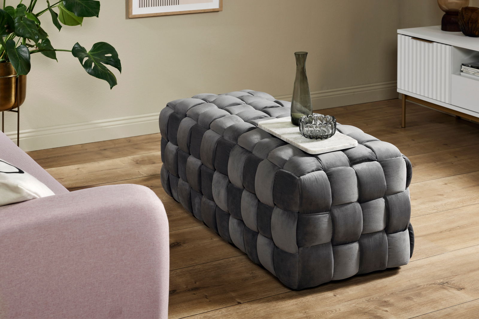 Grauer, gepolsterter Hocker in rechteckiger Form mit geflochtenem Design, seitliche Perspektive.