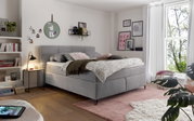 Gemütliches Boxspringbett in einem stilvoll eingerichteten Schlafzimmer, seitliche Perspektive mit Dekokissen und Decken.