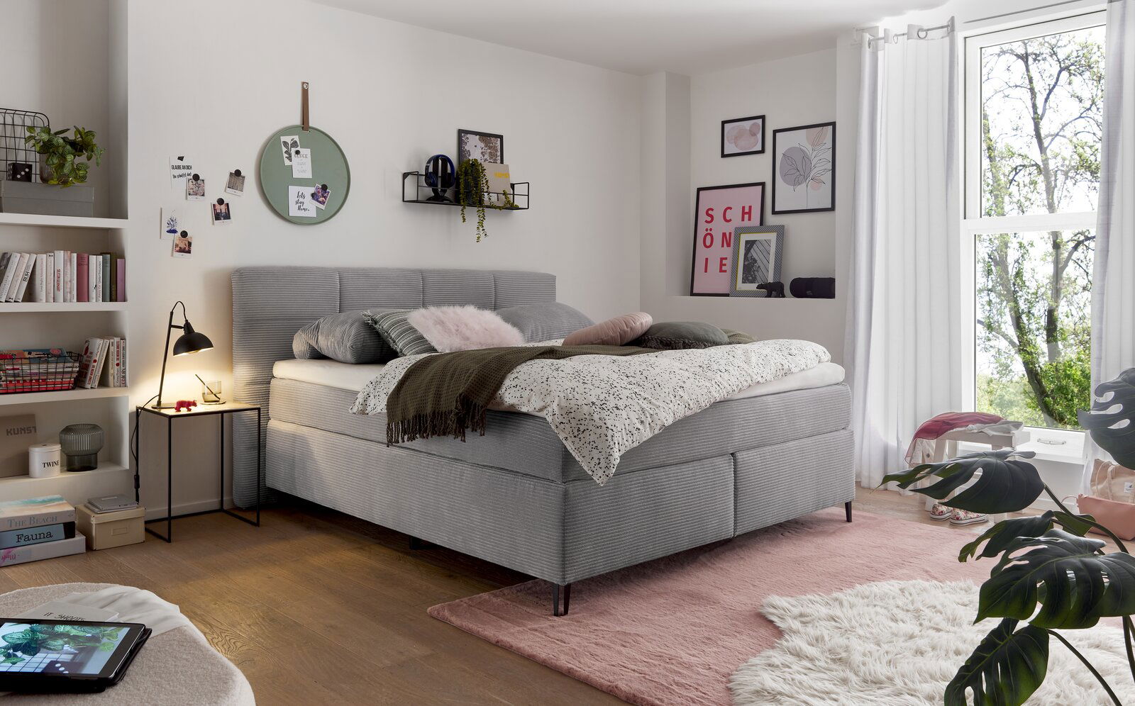 Gemütliches Boxspringbett in einem stilvoll eingerichteten Schlafzimmer, seitliche Perspektive mit Dekokissen und Decken.