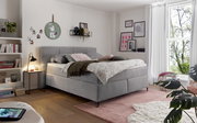 Gemütliches Boxspringbett in einem stilvoll eingerichteten Schlafzimmer, seitliche Perspektive mit Dekokissen und Decken.