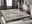 Moderner Designer Teppich in einem stilvollen Wohnzimmer, aus der Perspektive eines Sofas fotografiert. Der Teppich hat ein dezentes, graues Muster auf einem hellen Hintergrund und liegt auf einem dunklen Holzboden.