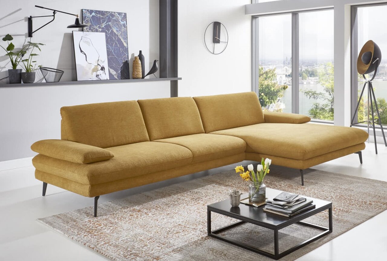 Gelbes Longchair-Sofa in modernem Wohnzimmer, seitliche Perspektive mit Blick auf große Fenster.