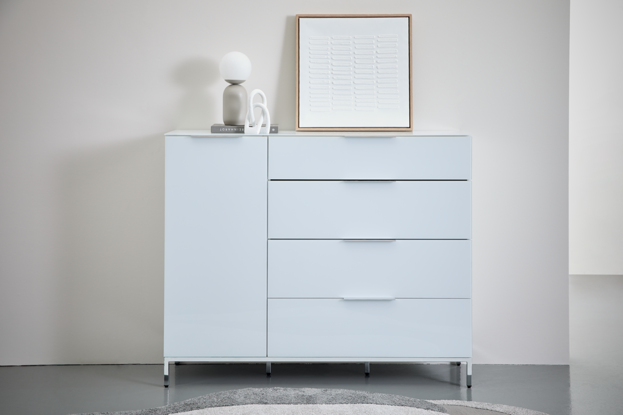 Novel Metalluntergestell 135 MALIN Moderne weiße Kommode mit Metalluntergestell, frontal fotografiert, dekoriert mit einer Lampe, Büchern und einem Kunstwerk.