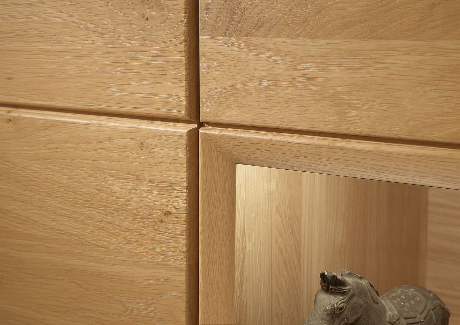 Nahaufnahme einer Wandkombination aus hellem Holz mit sichtbarer Maserung und einer dekorativen Skulptur im unteren Bereich.