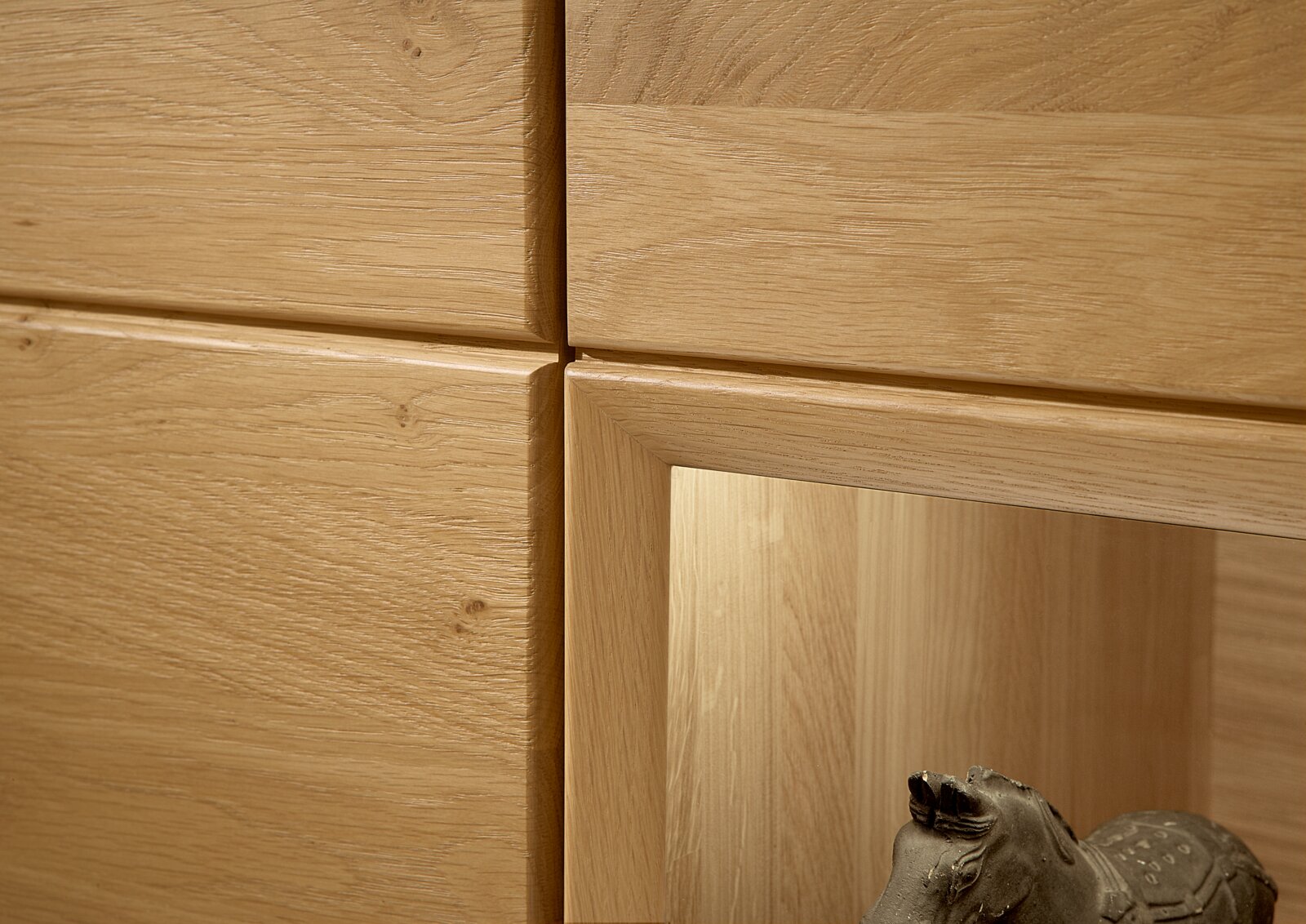 Close-up van een wandcombinatie van licht hout met zichtbare nerf en een decoratief beeldhouwwerk aan de onderkant.