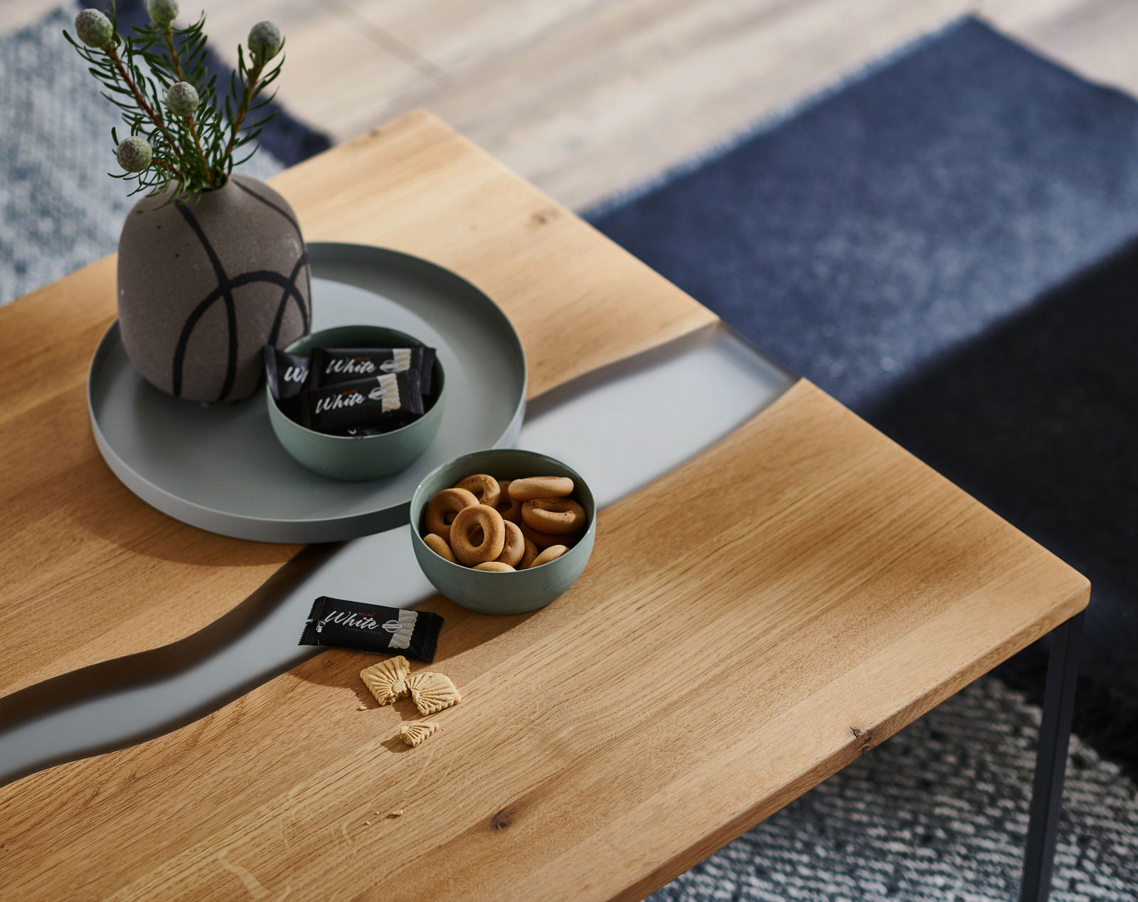 Moderner Couchtisch aus Holz mit dekorativem Einsatz, von oben fotografiert, mit Snacks und Vase dekoriert.