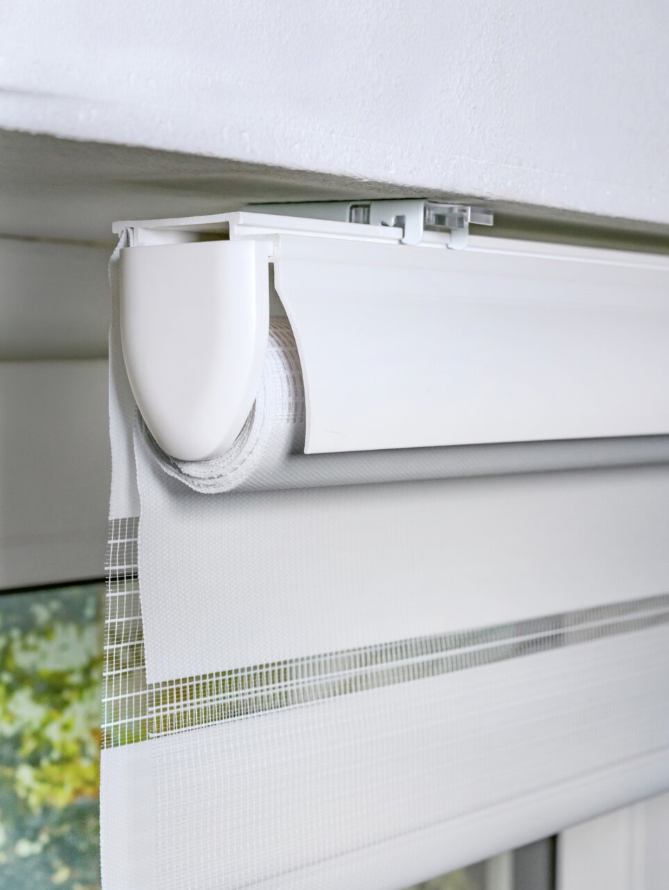 Nahaufnahme eines weißen Doppelrollos mit Blende, montiert an einer Decke, teilweise heruntergelassen.