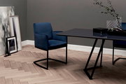 Freischwinger-Sessel in dunkelblauem Stoff, seitliche Perspektive, neben einem modernen Tisch in einem stilvollen Raum mit Holzboden.