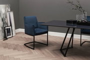Swingstoel in donkerblauwe stof, zijaanzicht, naast een moderne tafel in een stijlvolle ruimte met houten vloer.