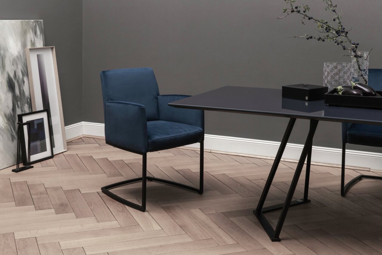 Swingstoel in donkerblauwe stof, zijaanzicht, naast een moderne tafel in een stijlvolle ruimte met houten vloer.