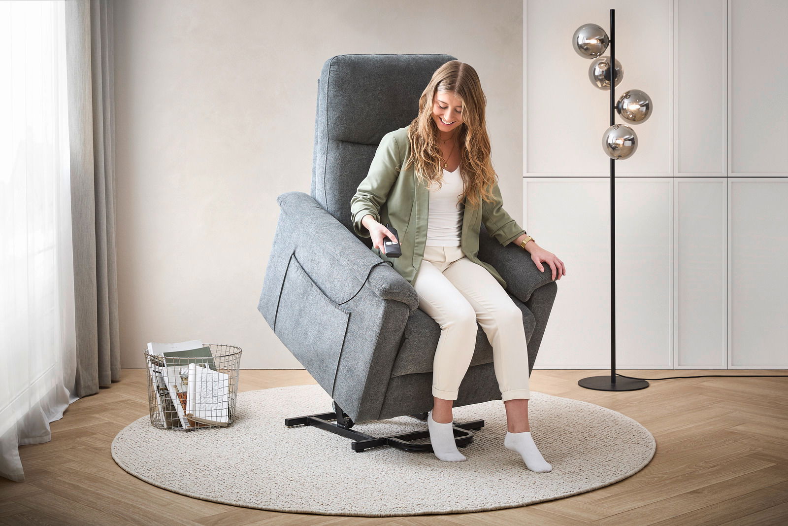 Frau sitzt in einem grauen Relaxsessel mit Fernbedienung, seitliche Perspektive