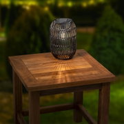 Een ijzeren zonne-lantaarn op een houten tafel, gefotografeerd vanuit een schuine hoek van bovenaf, met een warme gloed.