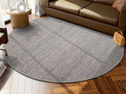 Runder, grauer Handwebteppich in einem modernen Wohnzimmer, auf einem Holzboden vor einem braunen Sofa platziert. Perspektive von oben.