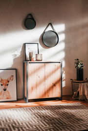 Kommode aus Holz mit Metallrahmen, frontal fotografiert, dekoriert mit Kerzen und einem Bild, in einem stilvoll eingerichteten Raum.