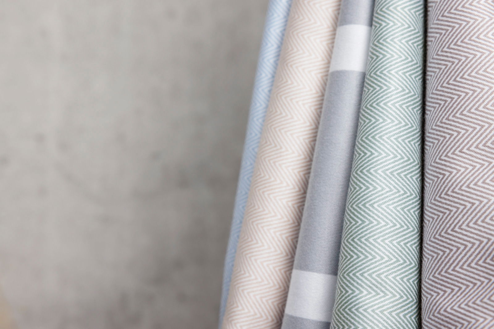 Nahaufnahme von mehreren Stoffrollen in verschiedenen Farben und Mustern, darunter Zickzack- und Streifenmuster, schräg angeordnet.