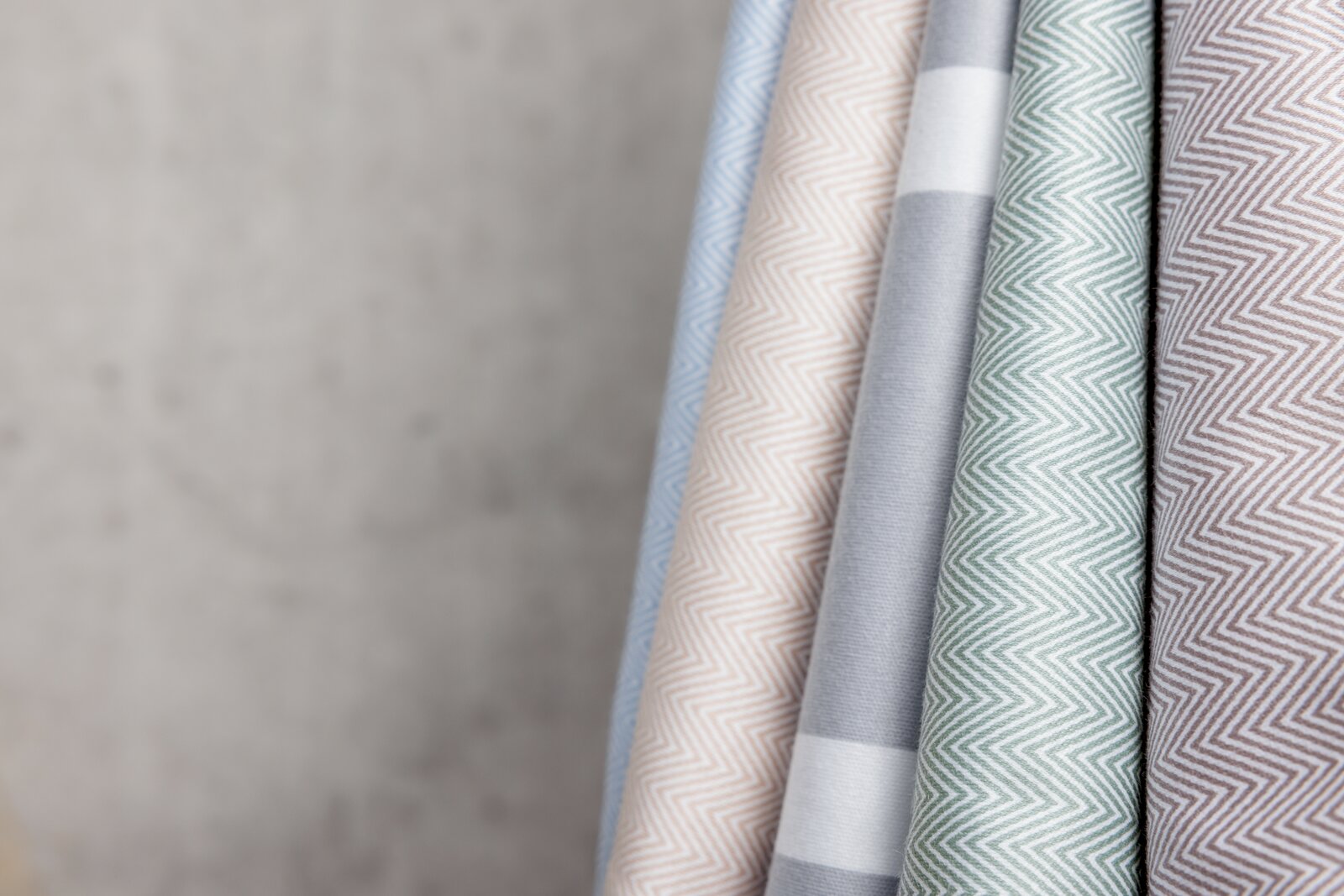 Nahaufnahme von mehreren Stoffrollen in verschiedenen Farben und Mustern, darunter Zickzack- und Streifenmuster, schräg angeordnet.