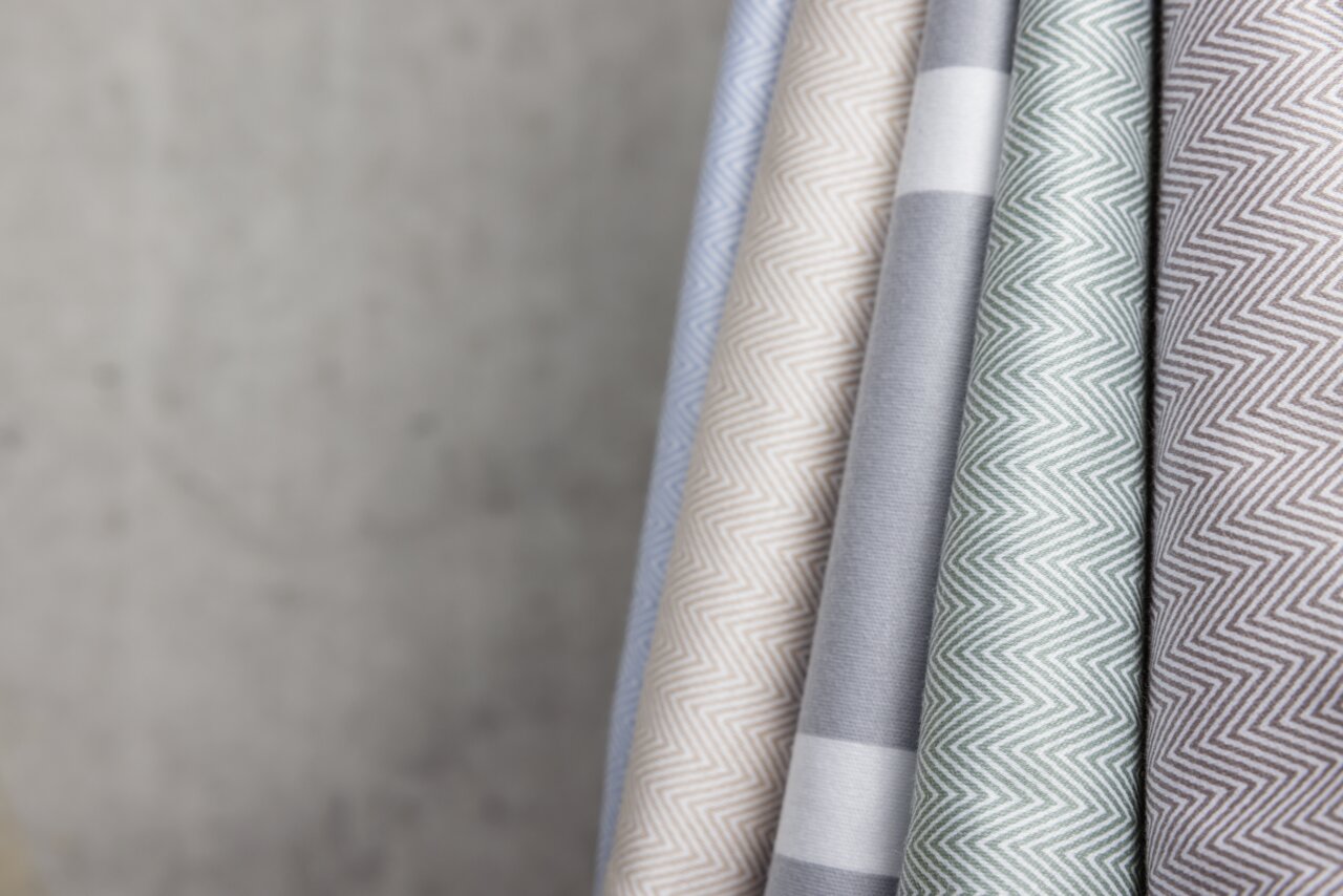 Nahaufnahme von mehreren Stoffrollen in verschiedenen Farben und Mustern, darunter Zickzack- und Streifenmuster, schräg angeordnet.