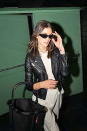 Frau in schwarzer Lederjacke und Sonnenbrille trägt einen schwarzen Einkaufskorb mit Griff, seitliche Perspektive.