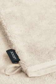 Nahaufnahme eines beigen Waschhandschuhs mit einem schwarzen Joop!-Etikett.