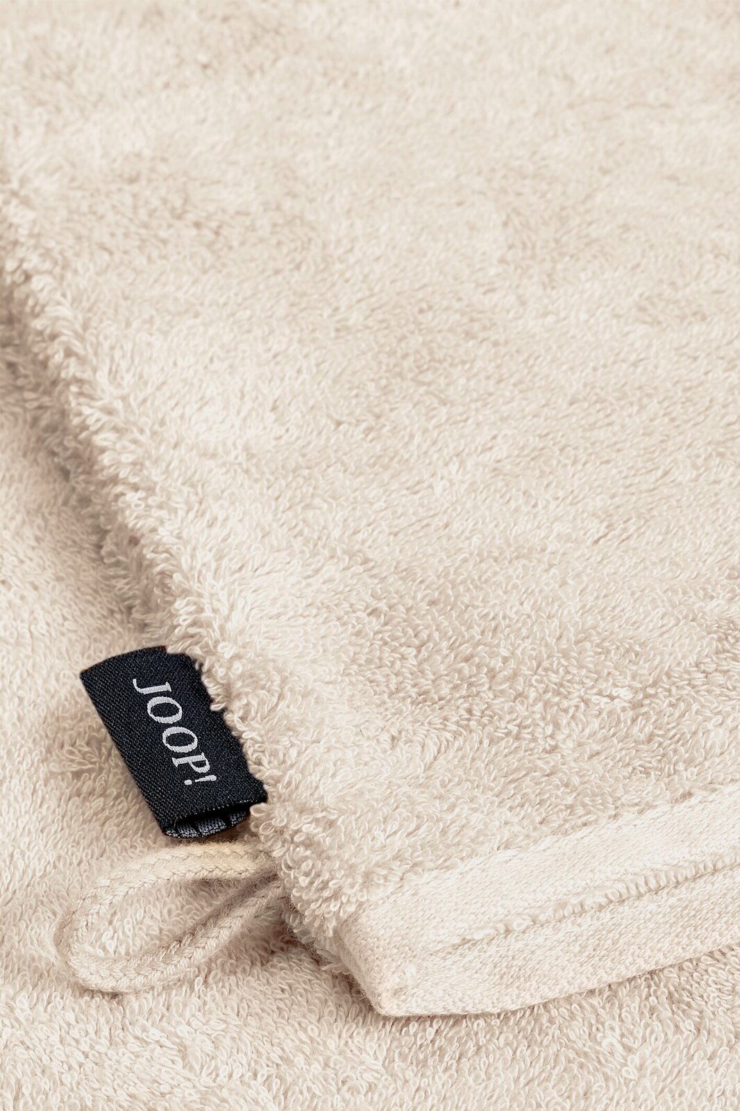 Nahaufnahme eines beigen Waschhandschuhs mit einem schwarzen Joop!-Etikett.