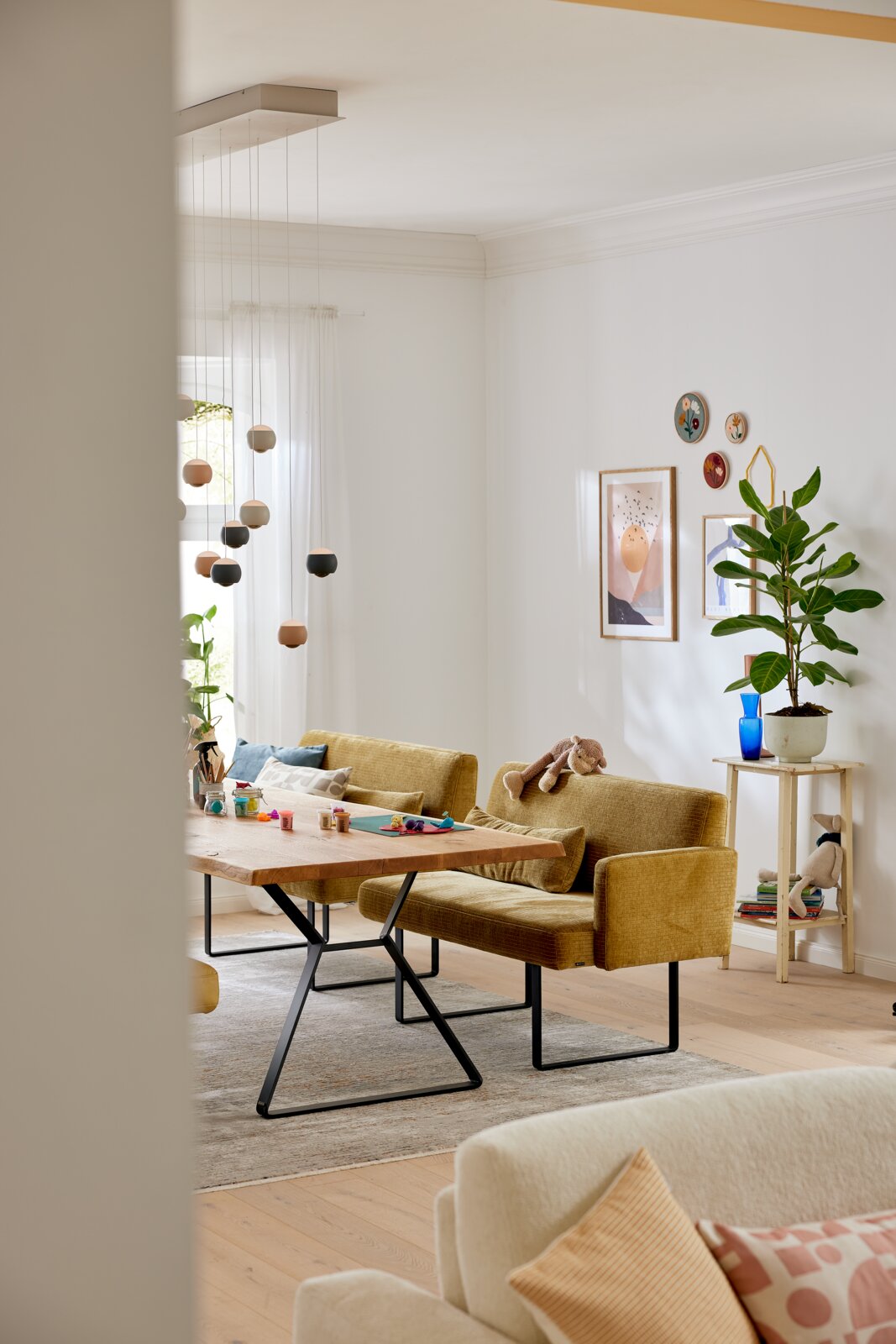 Gezellige eetkamerbank in mosterdgeel met armleuningen, gezien vanaf de zijkant, in een modern ingerichte ruimte met een houten tafel en decoraties.