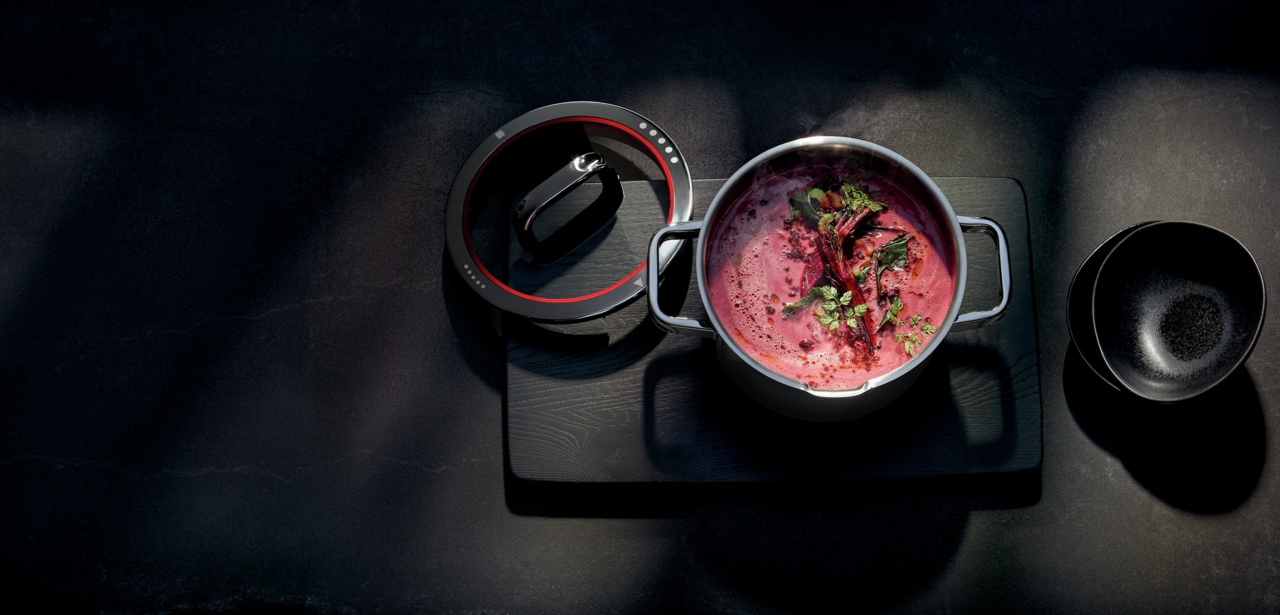 Bratentopf mit Deckel, gefüllt mit roter Suppe und Kräutern, aus der Vogelperspektive