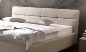 Beiges Polsterbett mit Kopfteil, seitlicher Blickwinkel, dekoriert mit Kissen und Decke.
