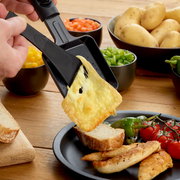 Nahaufnahme eines Raclette-Grills mit geschmolzenem Käse, der auf eine Brotscheibe gegossen wird. Im Hintergrund sind Schalen mit Gemüse und Kartoffeln zu sehen.
