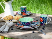 Buntes Geschirrset mit floral gemusterten Tassen, Schale und Tellern auf rustikalem Holztisch im Garten, mit Blaubeeren und Gebäck, fotografiert in leichter Draufsicht/Schrägansicht