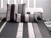 Bettwäsche-Set mit modernem Streifenmuster in Schwarz, Weiß und Grau, bestehend aus Kissen und Decke, auf einem weißen Sofa präsentiert.