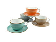 Vier gesprenkelte Keramik-Kaffeetassen mit Untertassen in Türkis, Orange, Grau und Beige auf weißem Hintergrund, schräg von vorne aus leicht erhöhter Perspektive fotografiert