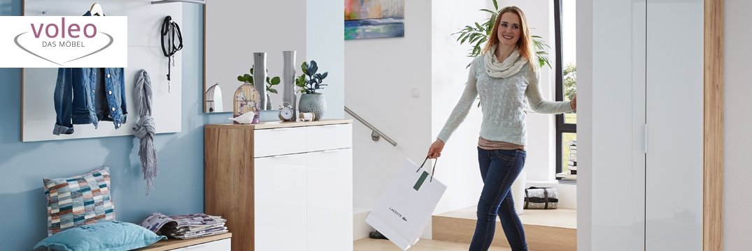 Eine Frau betritt einen modernen Flur mit Garderobe, Schuhschrank und gemütlicher Sitzbank mit Kissen.
