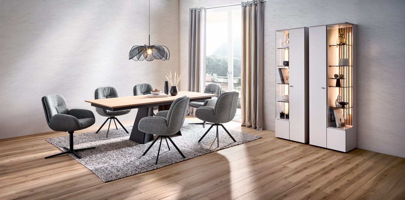 Venjakob Esstisch G37 Modernes Esszimmer-Set mit rechteckigem Holztisch, vier grauen Polsterstühlen auf Teppich, Pendelleuchte und beleuchteten weißen Vitrinenschränken neben bodentiefem Fenster, Perspektive: leicht schräg von vorn aus dem Raum
