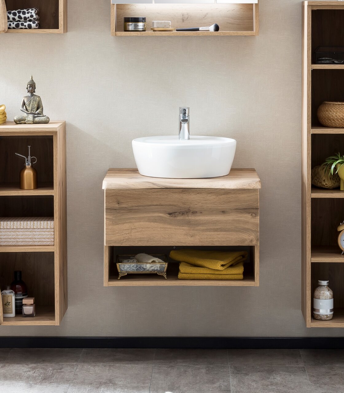 Moderner Waschtisch mit Holzoptik und weißem Aufsatzbecken, frontal fotografiert, umgeben von offenen Regalen mit Dekoration.