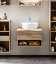 Moderner Waschtisch mit Holzoptik und weißem Aufsatzbecken, frontal fotografiert, umgeben von offenen Regalen mit Dekoration.