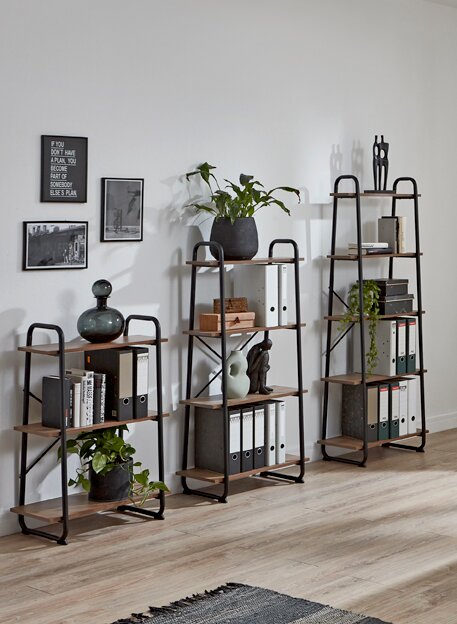 Drei industrielle Standregale aus schwarzem Metall und Holz mit Büchern, Ordnern und Pflanzen, frontal in einem hellen Wohnzimmer an der Wand arrangiert