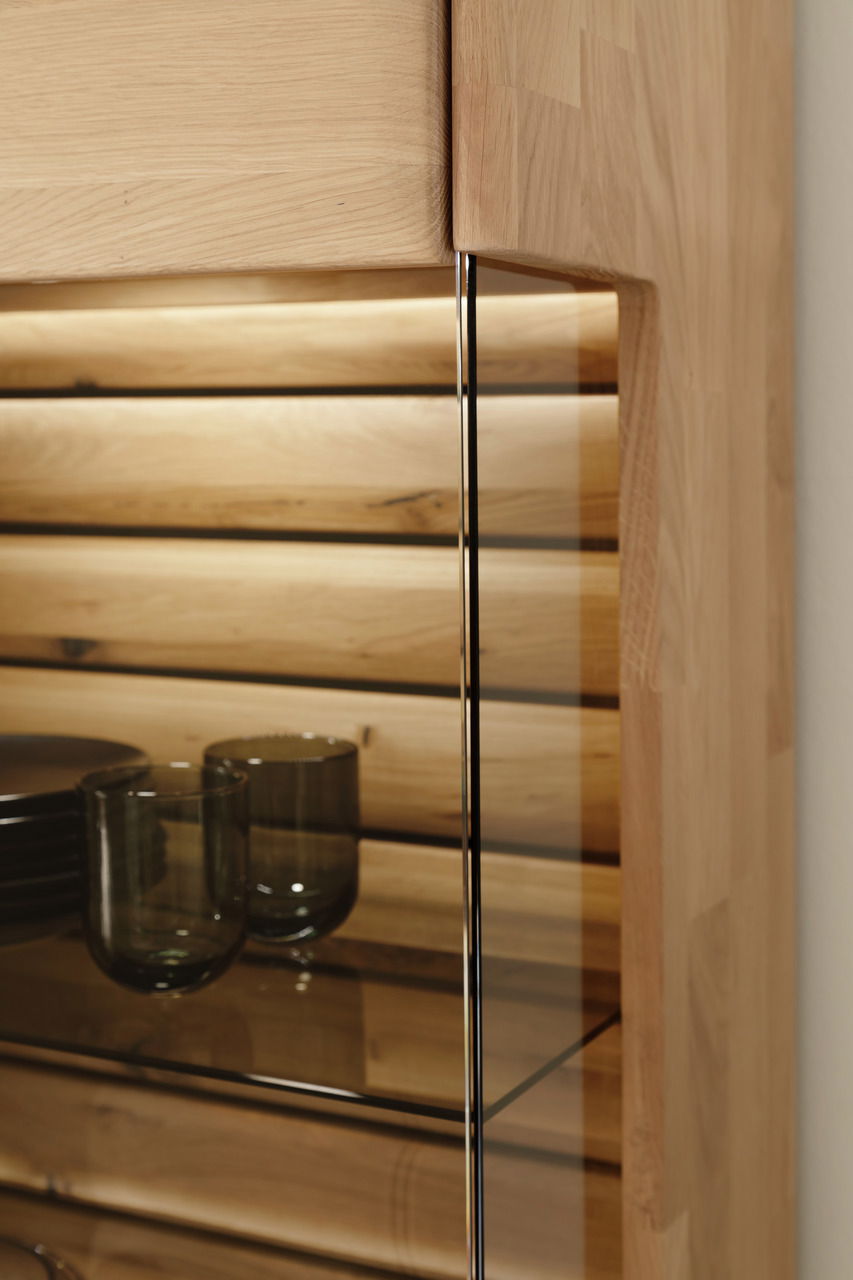 Detailansicht eines Highboards aus Holz mit Glasregalen und LED-Beleuchtung, Perspektive von der Seite.