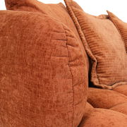 Nahaufnahme eines Big-Sofas in warmem Terrakotta-Ton mit weichen, strukturierten Kissen, seitliche Perspektive.