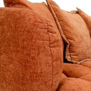 Nahaufnahme eines Big-Sofas in warmem Terrakotta-Ton mit weichen, strukturierten Kissen, seitliche Perspektive.