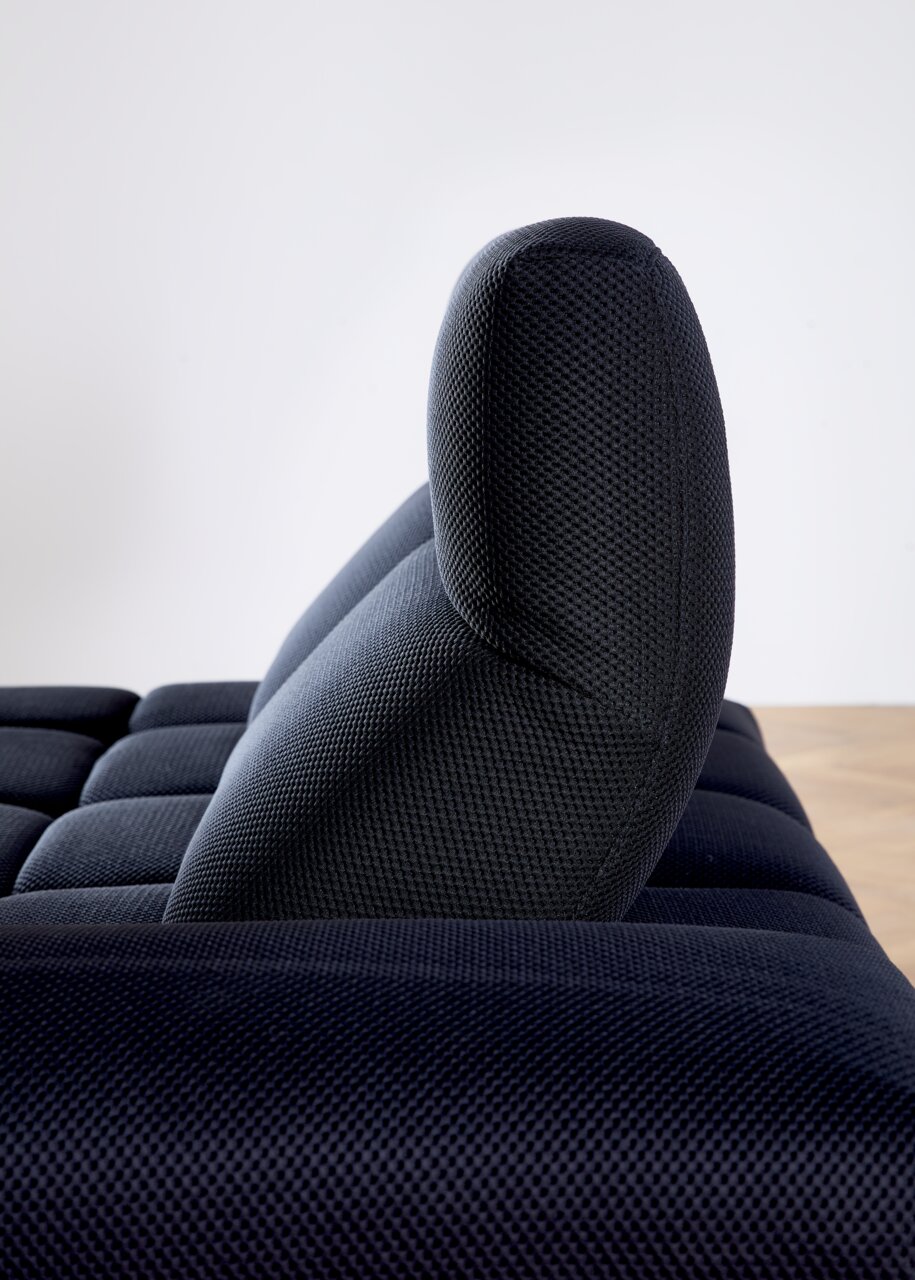 Zijaanzicht van een donkerblauwe hoekbank met een gestructureerd oppervlak en een gestoffeerde rugleuning.